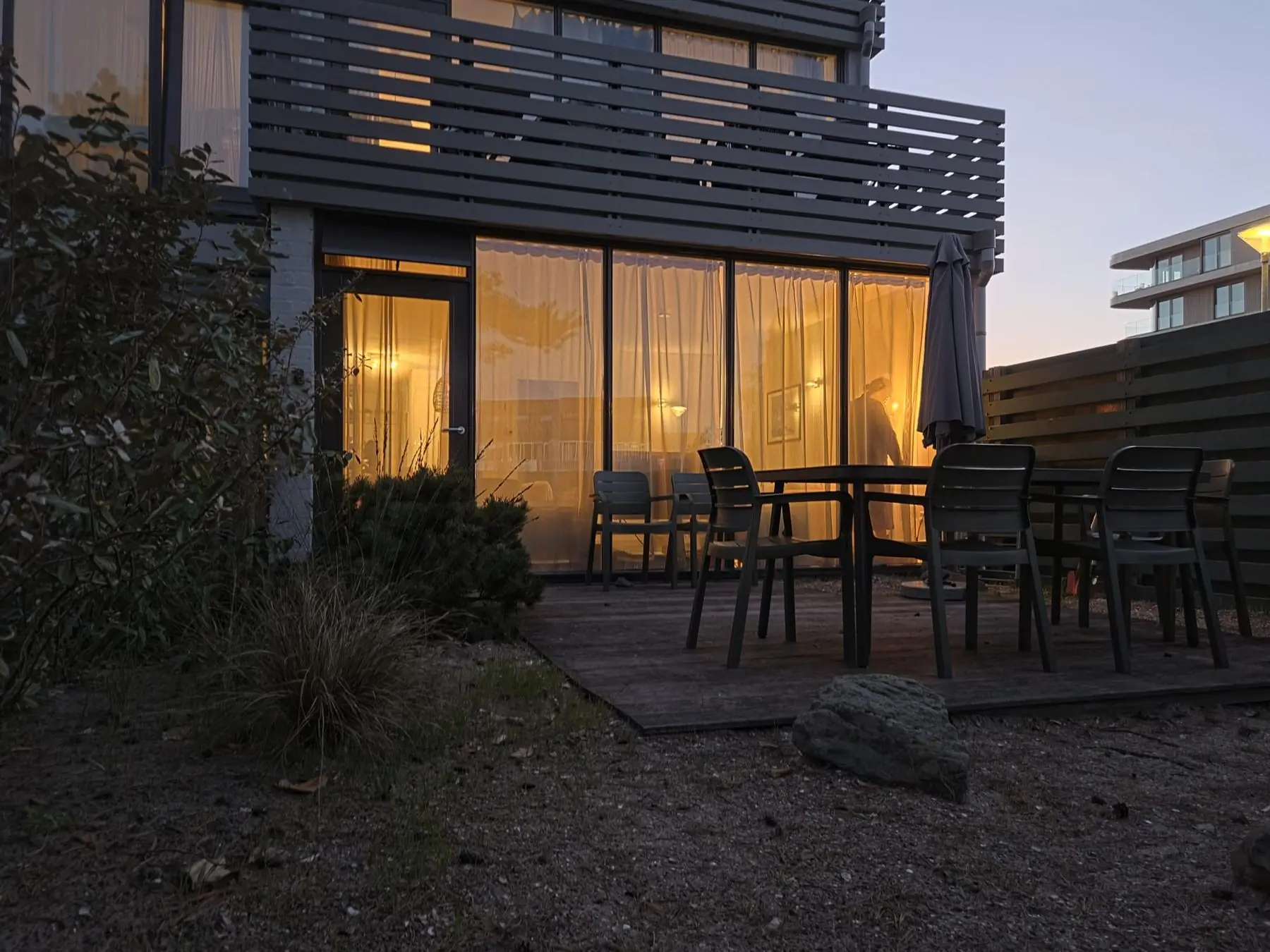 De tuin bij schemering, met warm licht achter de ramen