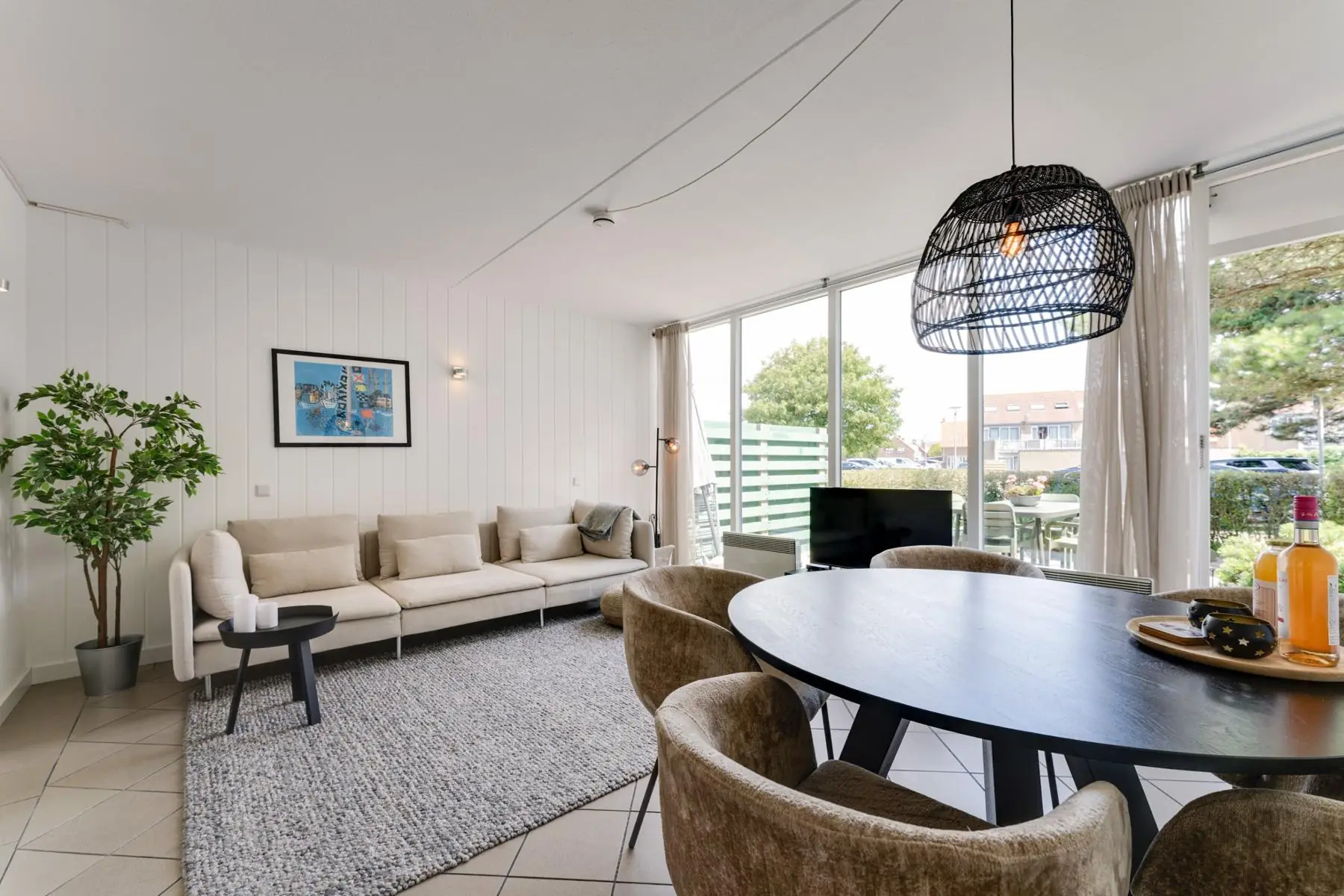 Woonkamer met lichte bank, ronde eettafel en grote ramen