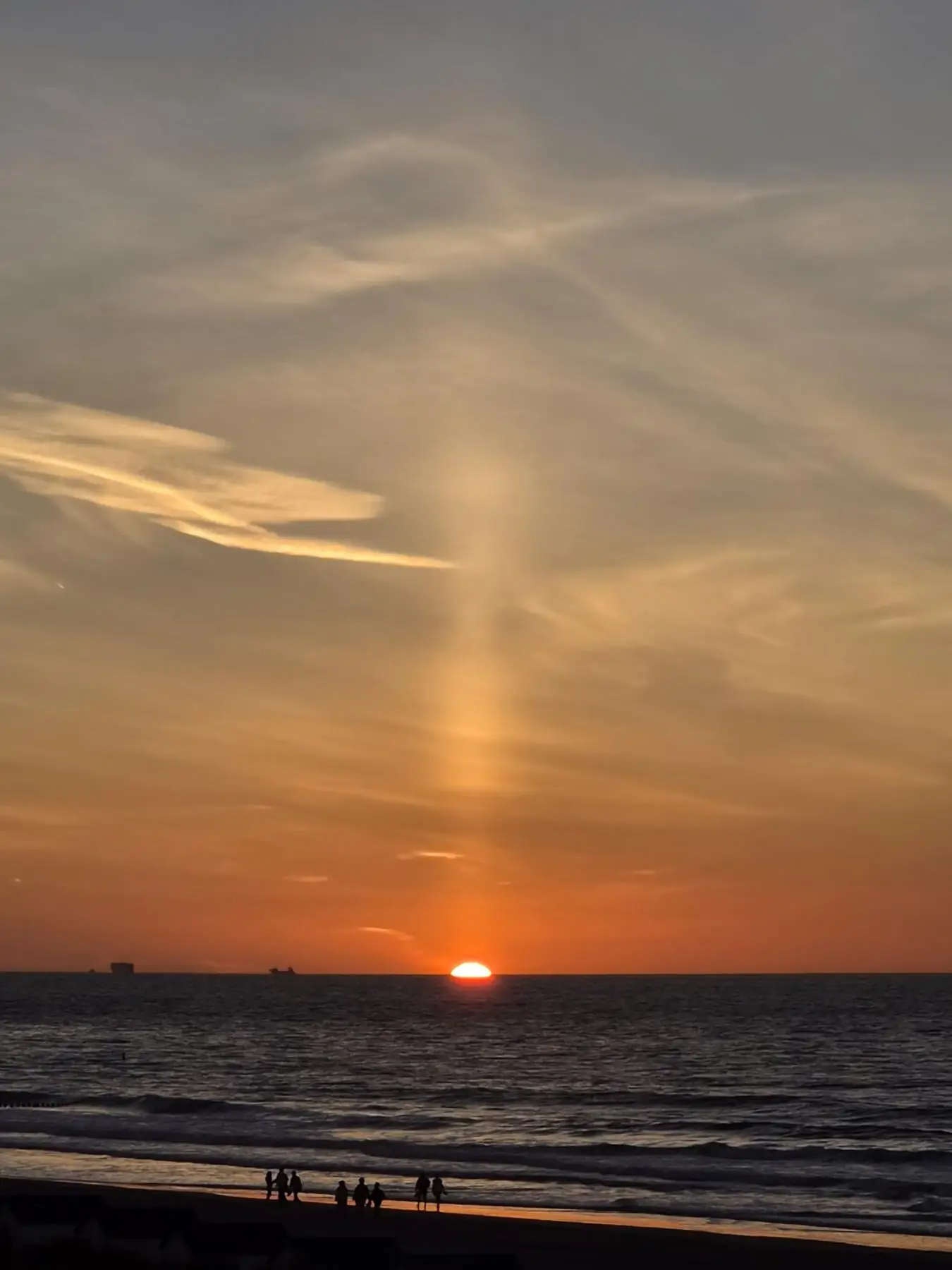 Zonsondergang boven de Noordzee met wandelaars op het strand